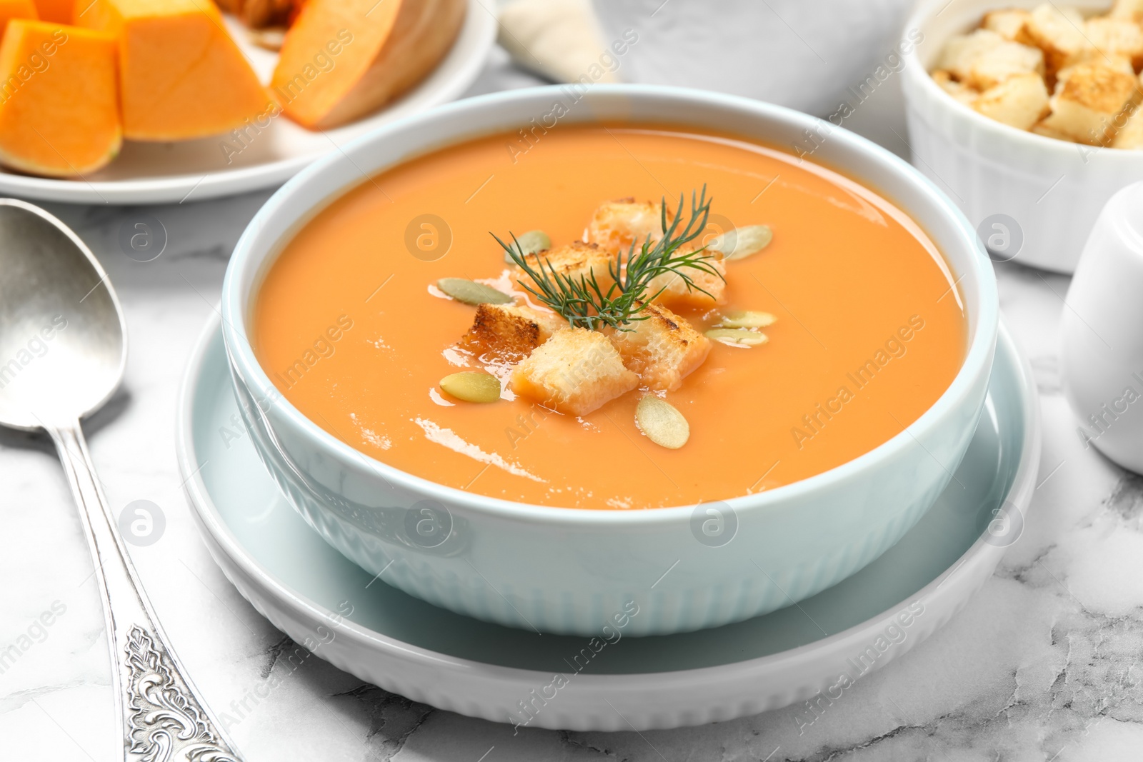 Photo of Tasty creamy pumpkin soup with croutons, seeds and dill in bowl on white marble table