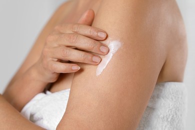Woman applying body cream onto arm on grey background, closeup