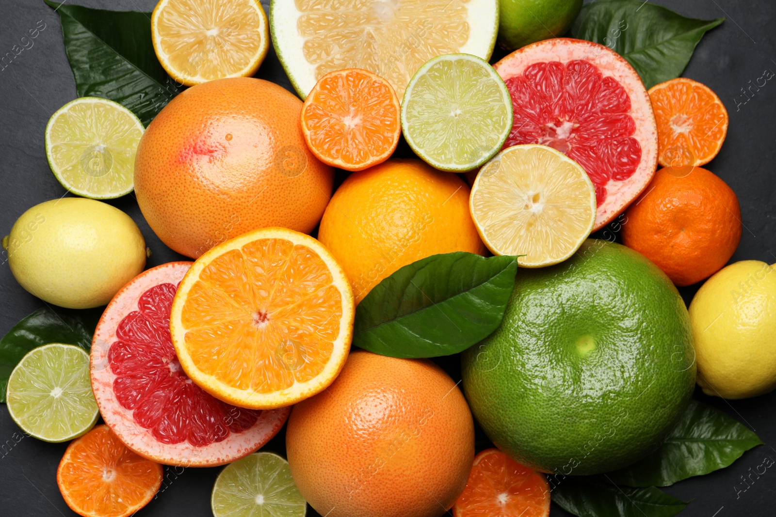 Photo of Different ripe citrus fruits with green leaves on black table, flat lay