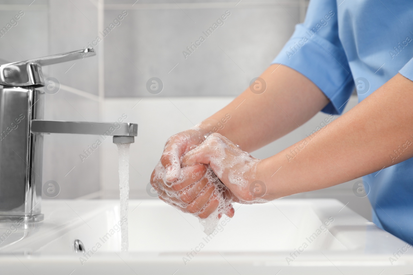 Photo of Doctor washing hands with water from tap in bathroom, closeup