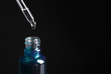 Dripping cosmetic serum from pipette into bottle on black background, space for text