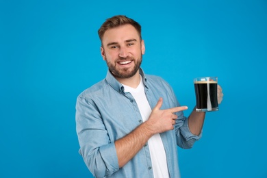 Handsome man with cold kvass on blue background. Traditional Russian summer drink