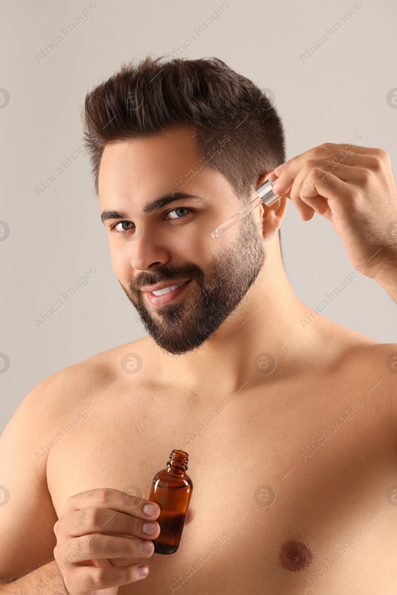 Photo of Handsome man applying cosmetic serum onto face on light grey background