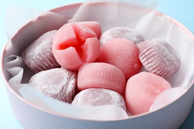 Photo of Many different delicious mochi in box on light blue background, closeup. Traditional Japanese dessert