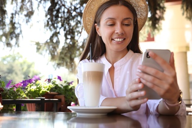 Photo of Beautiful young woman with coffee and smartphone at table in outdoor cafe