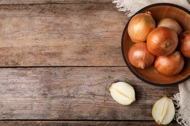 Photo of Flat lay composition with bowl of ripe onions on wooden table, space for text