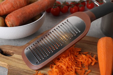 Hand grater and fresh ripe carrot on wooden board, closeup