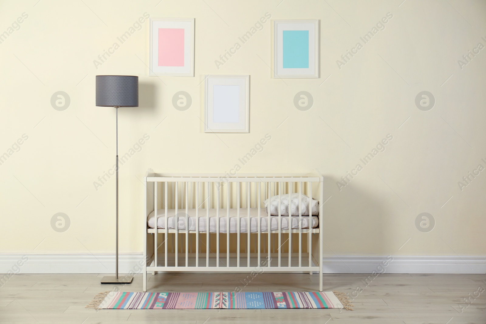 Photo of Crib and floor lamp near light wall in baby room interior