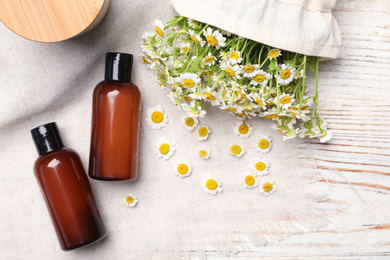 Flat lay composition with chamomile flowers and cosmetic products on white wooden table