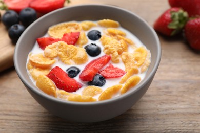Bowl of tasty crispy corn flakes with milk and berries on wooden table, closeup
