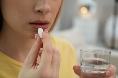 Photo of Young woman taking abortion pill on blurred background, closeup