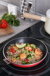Photo of Tasty rice with shrimps and vegetables in frying pan on induction stove, space for text