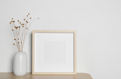 Photo of Empty photo frame and vase with dry decorative flowers on wooden table. Mockup for design