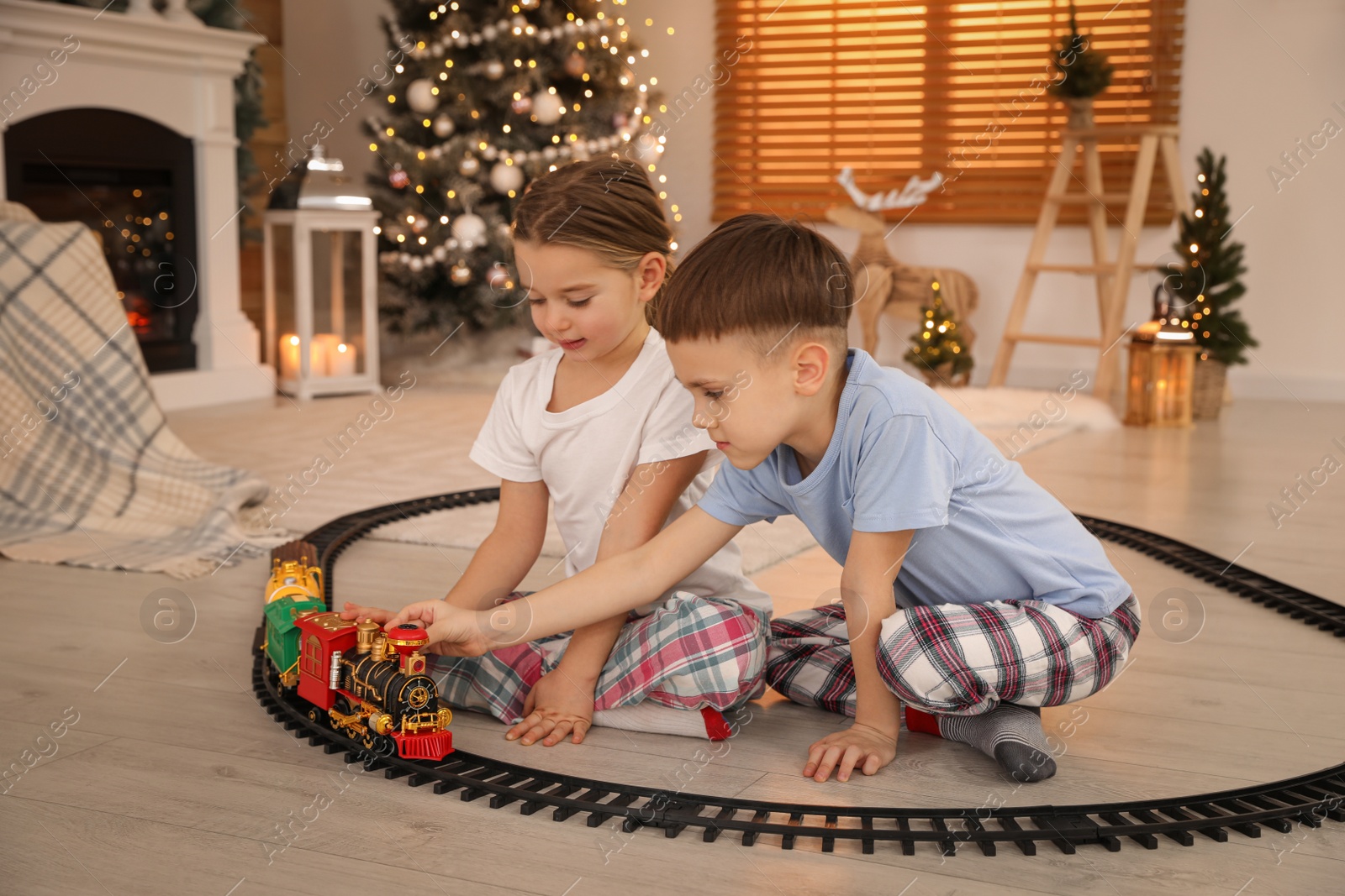 Photo of Children playing with colorful train toy in room decorated for Christmas