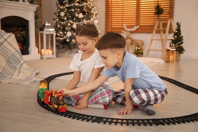 Photo of Children playing with colorful train toy in room decorated for Christmas
