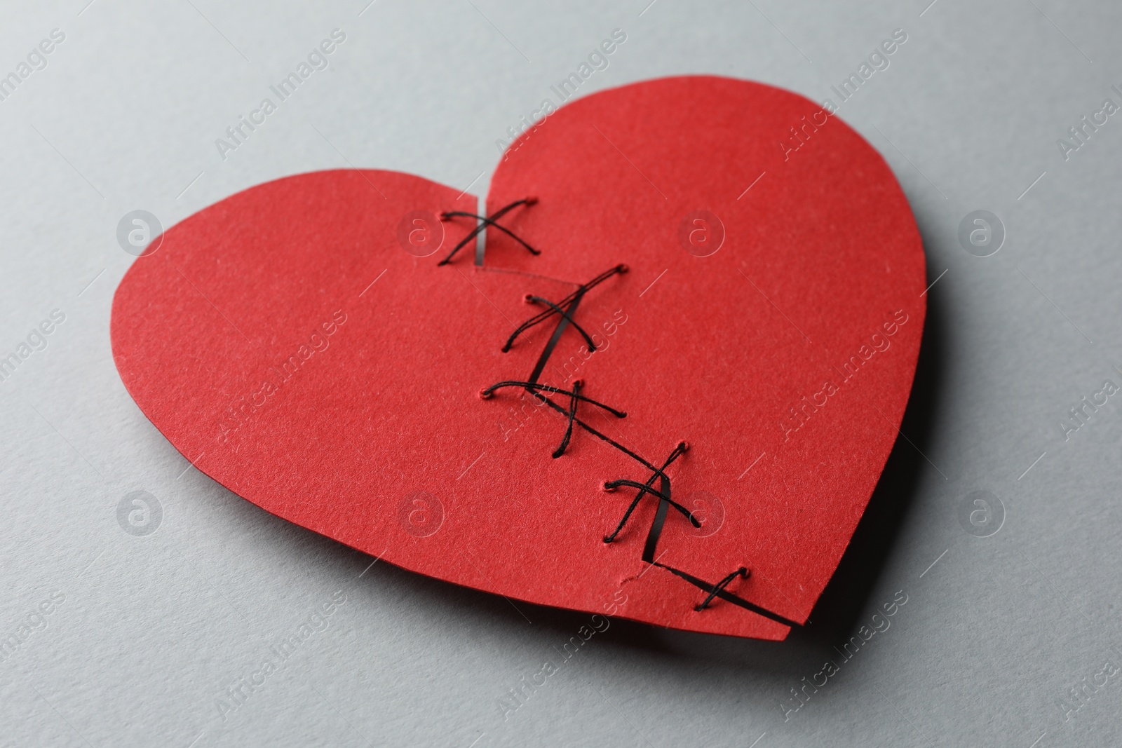 Photo of Broken heart. Torn red paper heart sewed with thread on light grey background, closeup