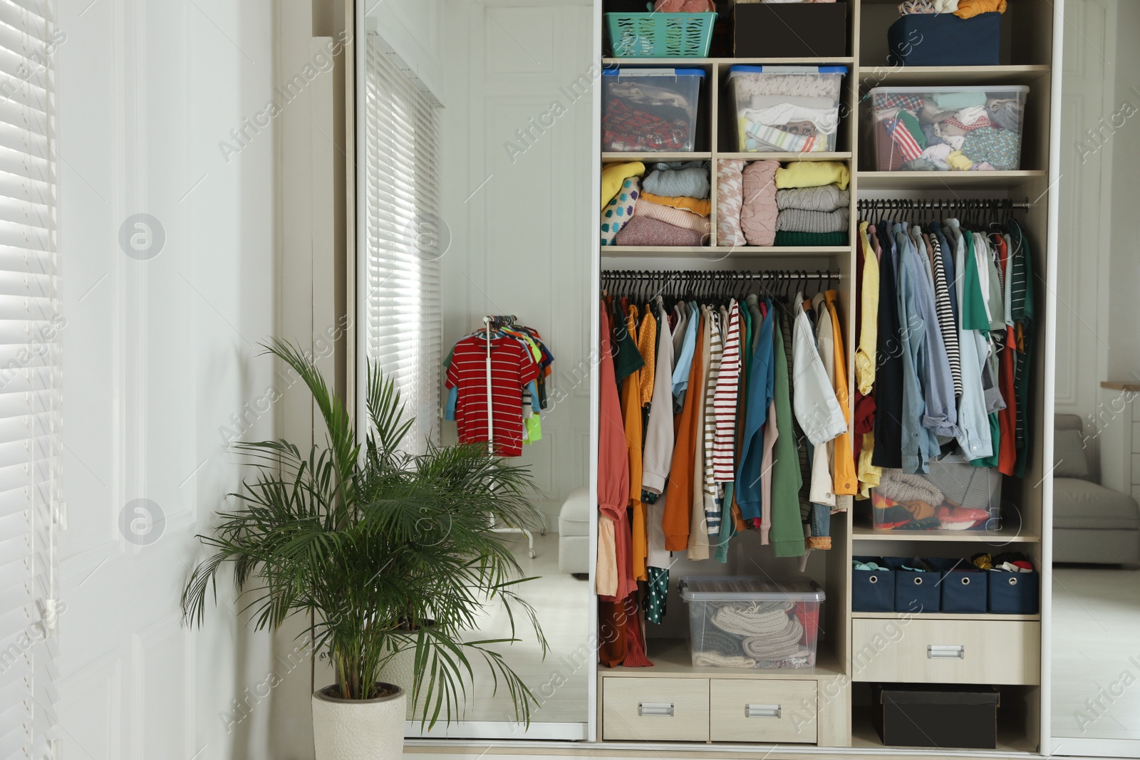 Photo of Wardrobe closet with different stylish clothes and home stuff in room. Fast fashion