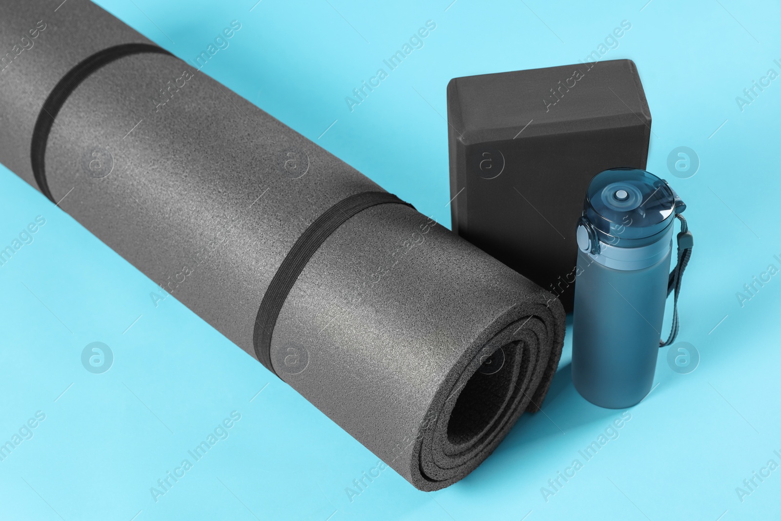 Photo of Exercise mat, yoga block and bottle of water on light blue background