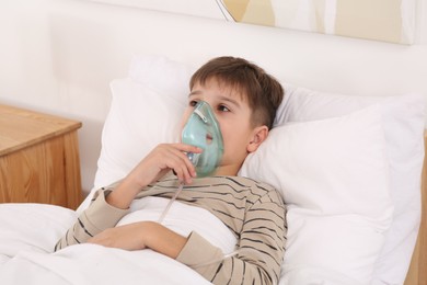 Boy using nebulizer for inhalation on bed at home