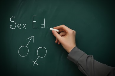 Image of Woman writing words Sexual Education on green chalkboard, closeup. Chalked female and male gender signs