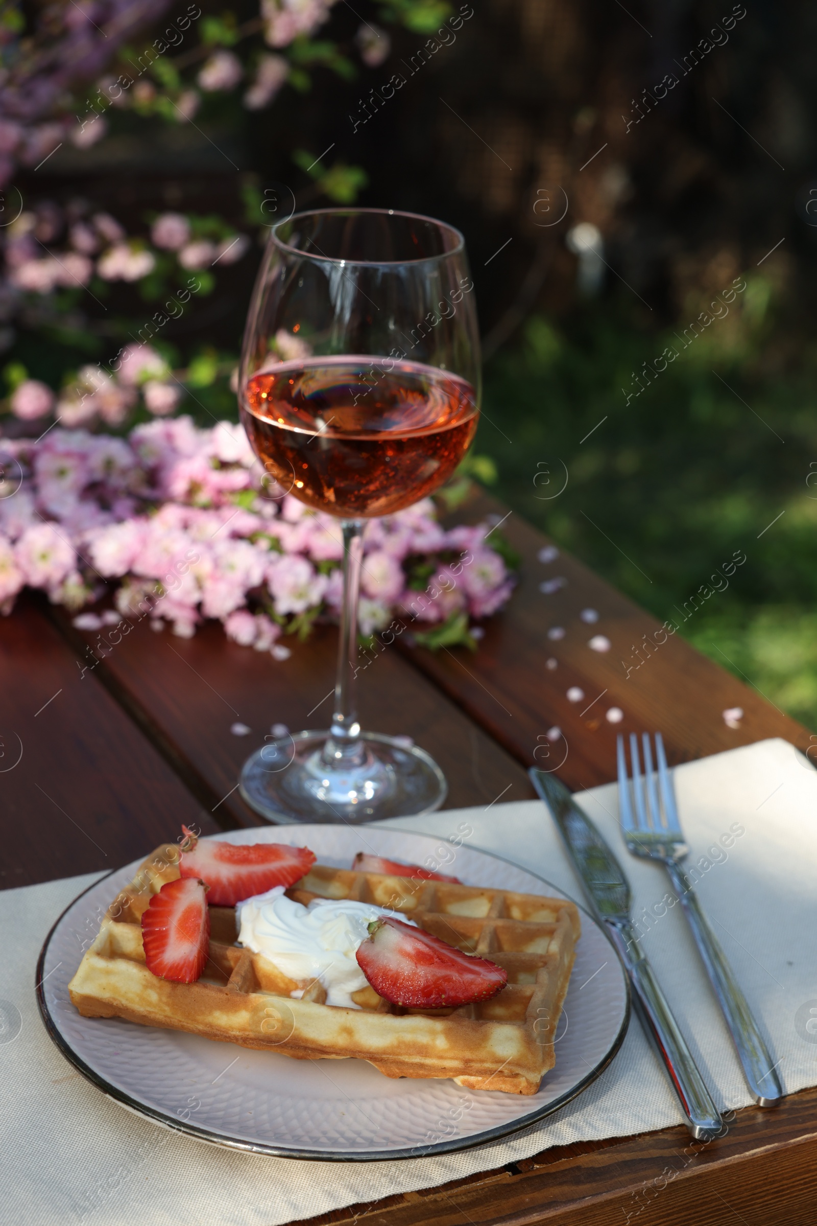 Photo of Delicious Belgian waffles with fresh strawberries and wine served on table in spring garden