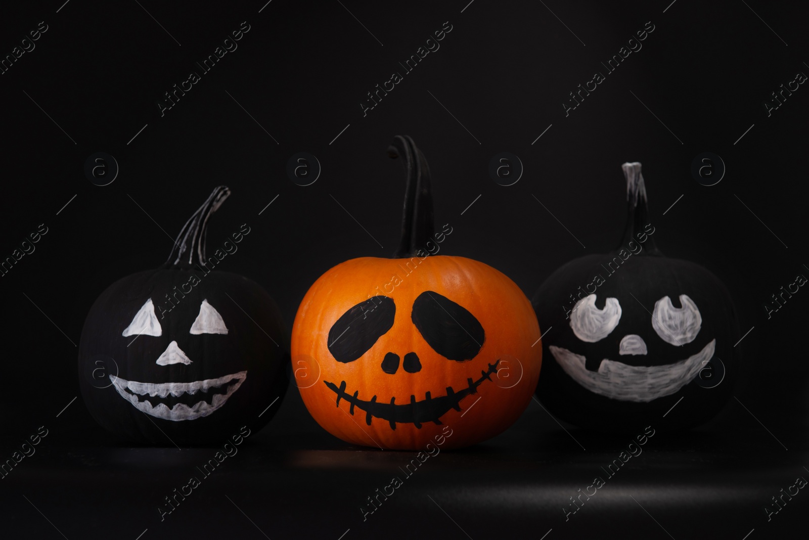 Photo of Halloween celebration. Pumpkins with drawn faces on table in darkness