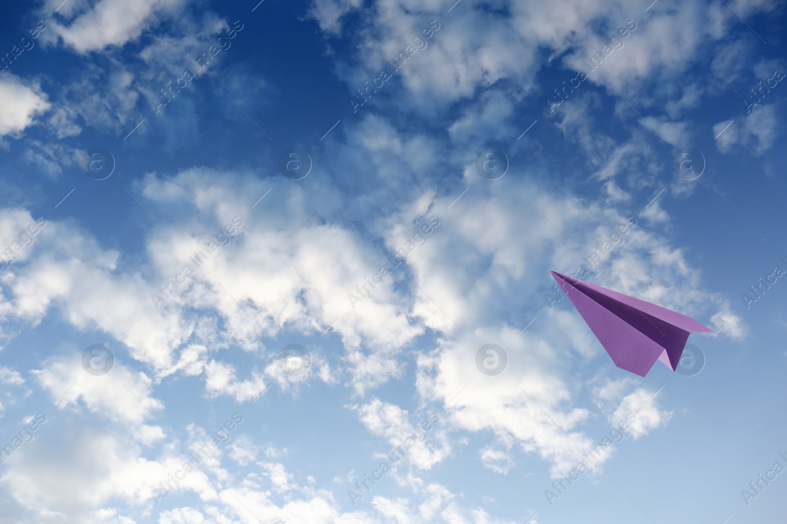 Image of Purple paper plane flying in blue sky with clouds