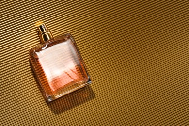Photo of Luxury women's perfume. Sunlit glass bottle on golden surface, top view. Space for text