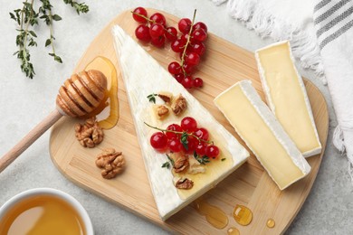 Photo of Brie cheese served with red currants, walnuts and honey on light table, flat lay