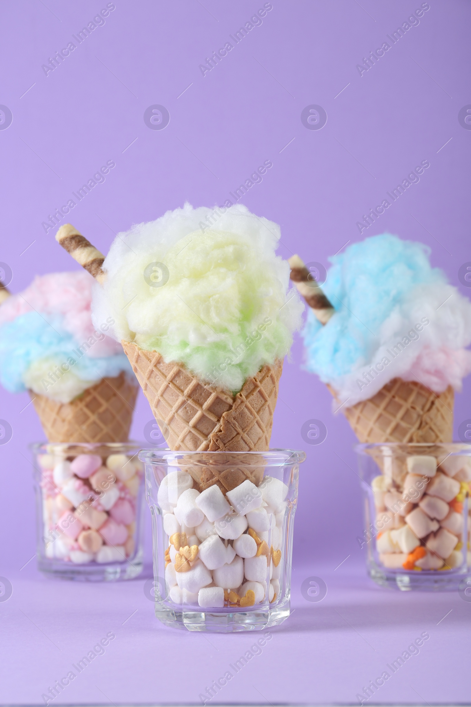 Photo of Sweet cotton candies in waffle cones on purple background