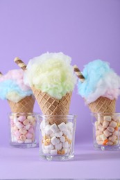 Photo of Sweet cotton candies in waffle cones on purple background