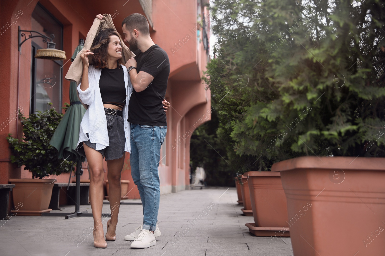 Photo of Young couple enjoying time together under rain on city street, space for text