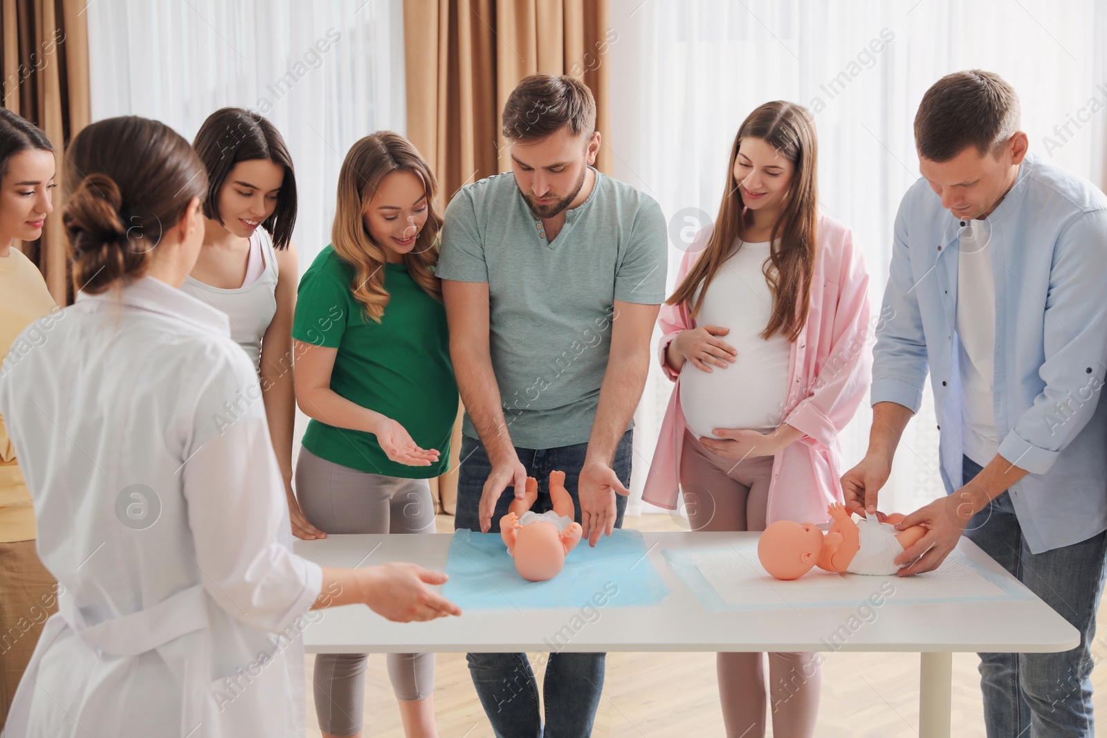 Photo of Future fathers and pregnant women learning how to swaddle baby at courses for expectant parents indoors