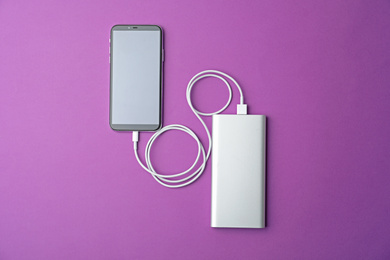 Photo of Smartphone and portable charger on purple background, flat lay. Modern technology