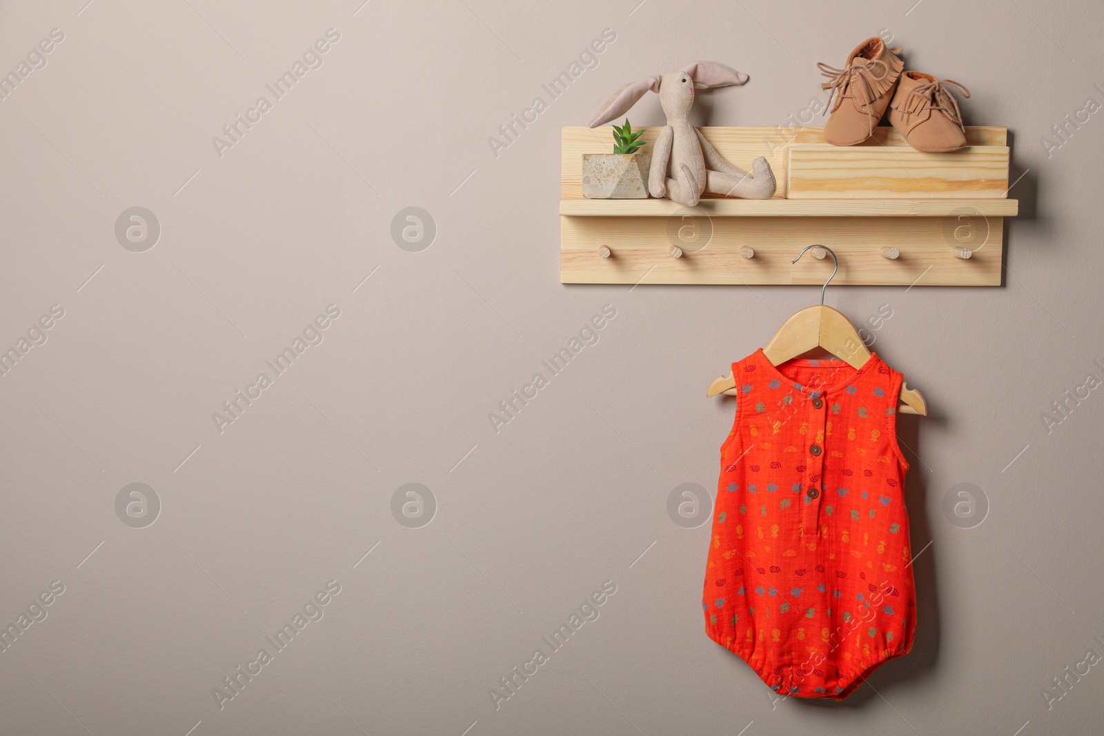 Photo of Baby bodysuit, booties and toy on wooden rack. Space for text