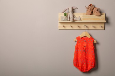 Baby bodysuit, booties and toy on wooden rack. Space for text