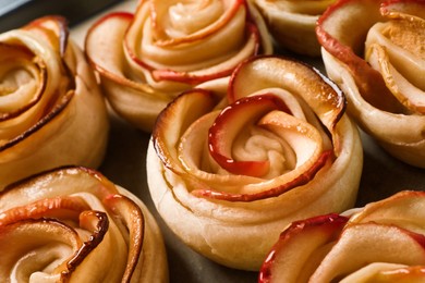 Photo of Freshly baked apple roses on parchment paper, closeup. Beautiful dessert