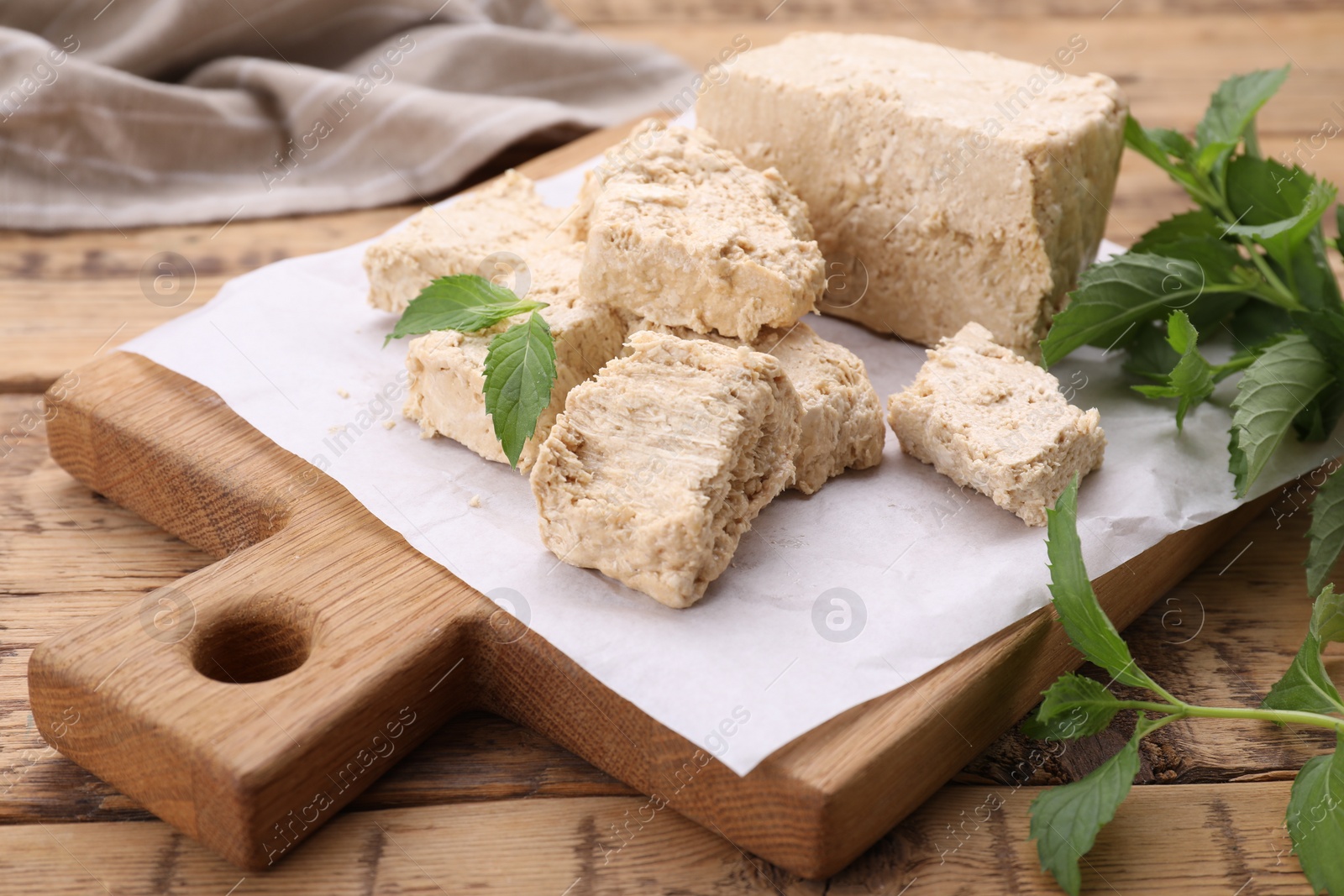 Photo of Pieces of tasty halva and mint leaves on wooden table, closeup