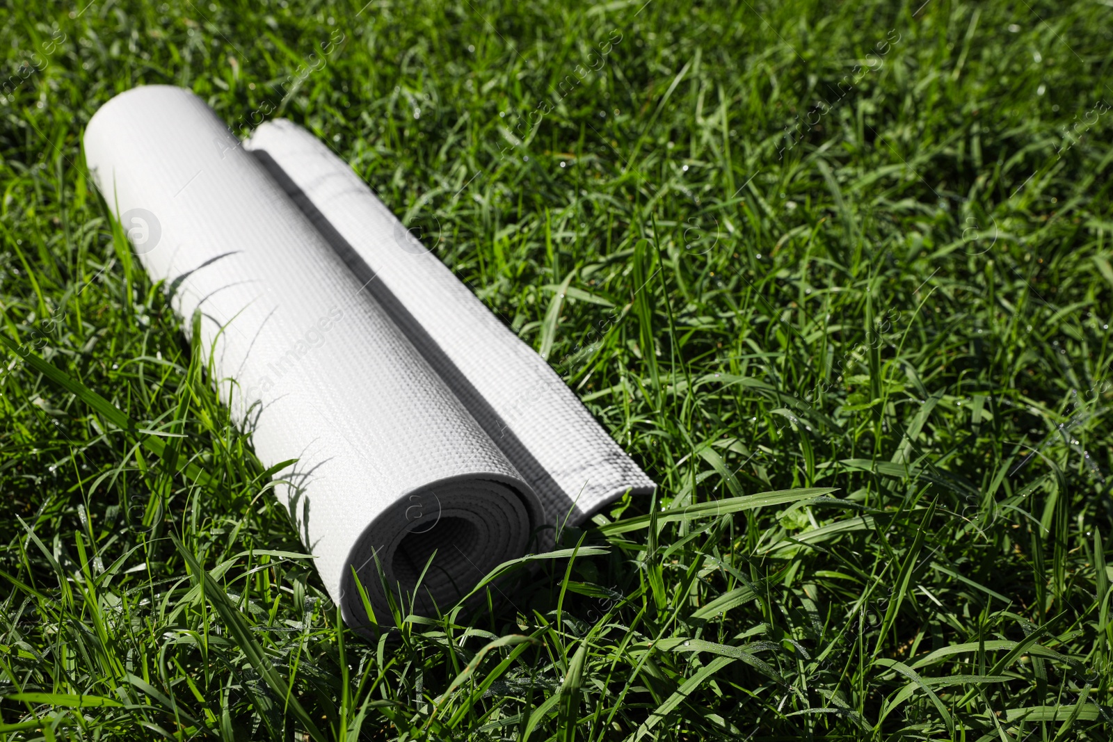 Photo of Rolled karemat or fitness mat on green grass outdoors, space for text