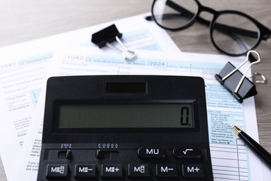 Photo of Tax accounting. Calculator, documents, glasses and stationery on wooden table, closeup