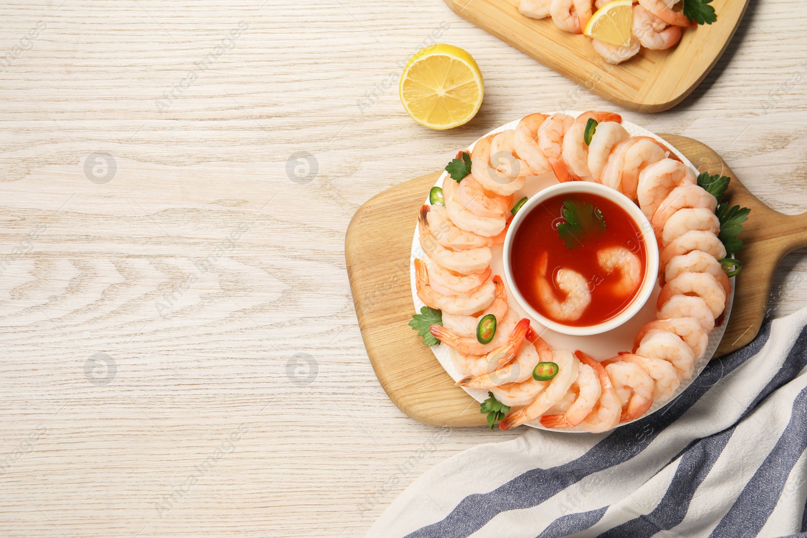 Photo of Tasty boiled shrimps with cocktail sauce, chili and parsley on light wooden table, top view. Space for text