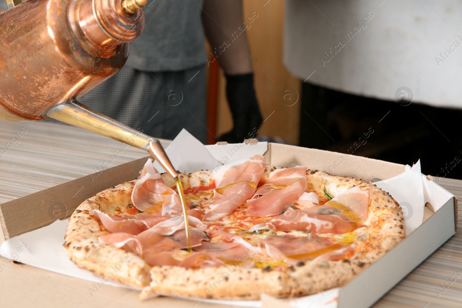 Photo of Professional chef pouring olive oil onto Italian oven baked pizza in restaurant, closeup