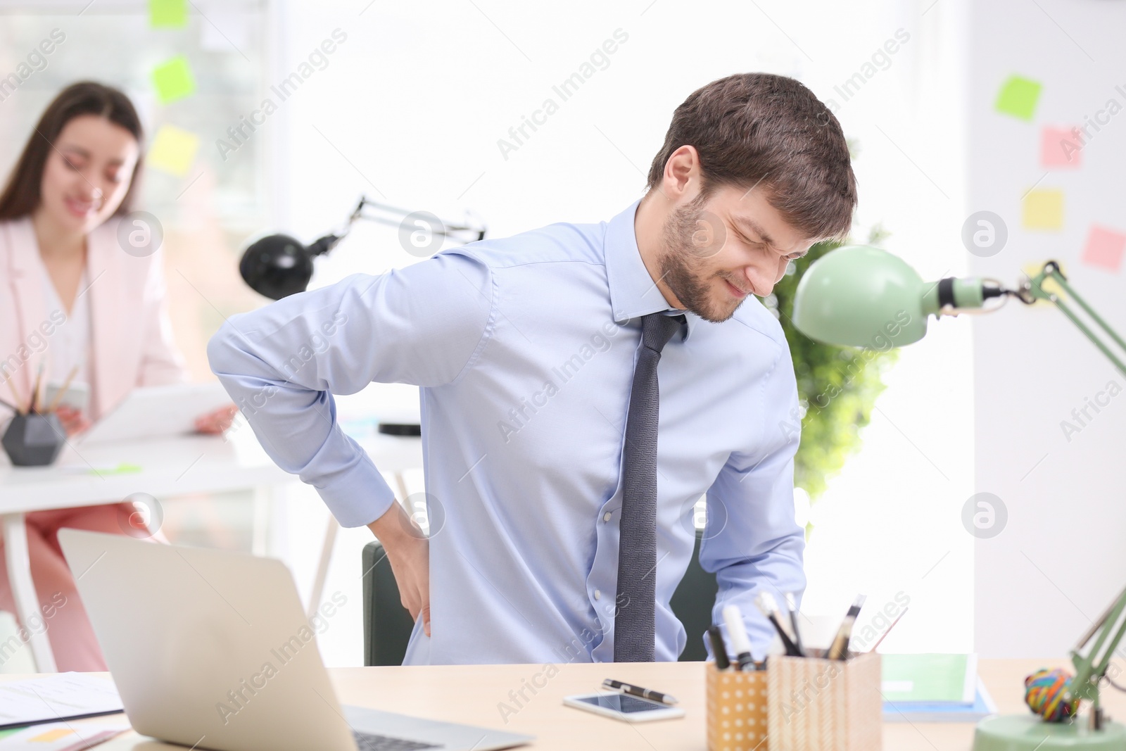 Photo of Young man suffering from back pain in office