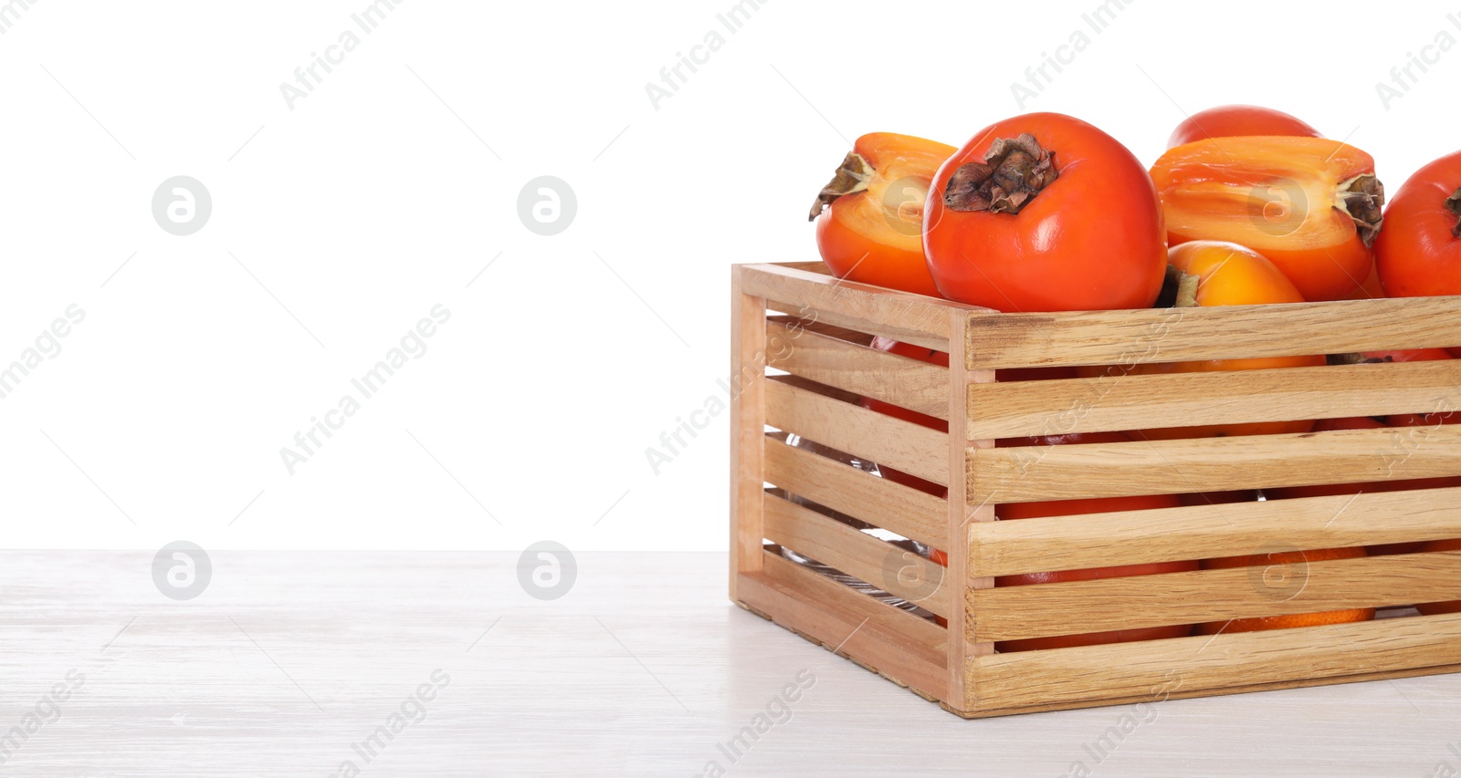 Photo of Delicious ripe juicy persimmons in crate on wooden table against white background