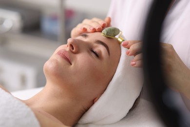 Cosmetologist making face massage with roller to client in clinic, closeup