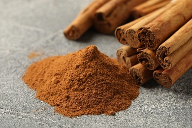 Photo of Cinnamon powder and sticks on grey table, closeup