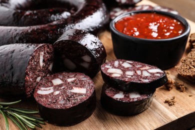 Tasty blood sausages with rosemary and sauce on wooden board, closeup