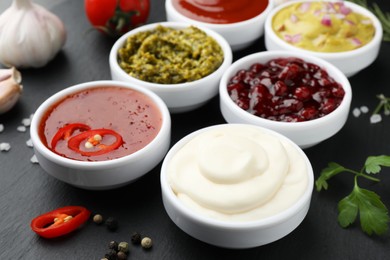 Different tasty sauces in bowls and ingredients on black table, closeup