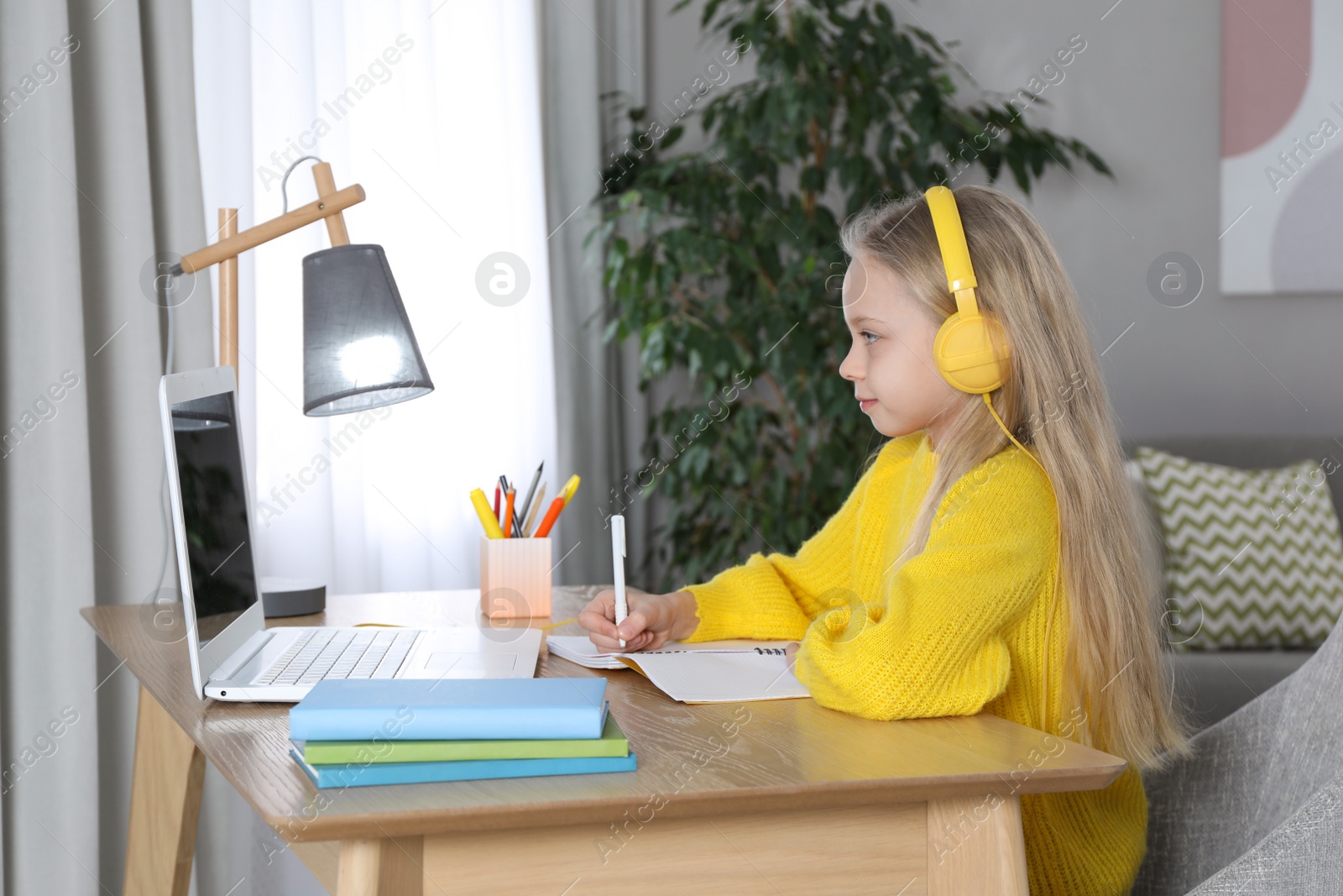 Photo of Cute little girl with modern laptop studying online at home. E-learning