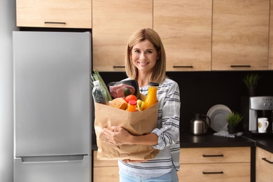 Woman with paper bag full of products near refrigerator in kitchen